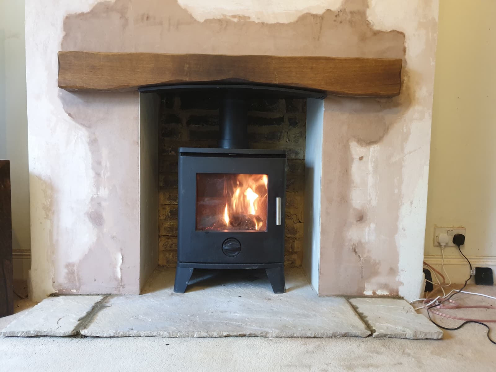 Wood burning stove in a plastered chimney breast finished with a reclaimed oak beam