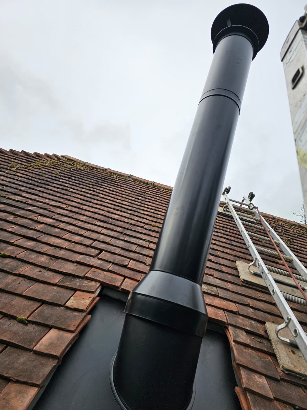 Close-up of a black twin-wall flue passing through a tiled roof line