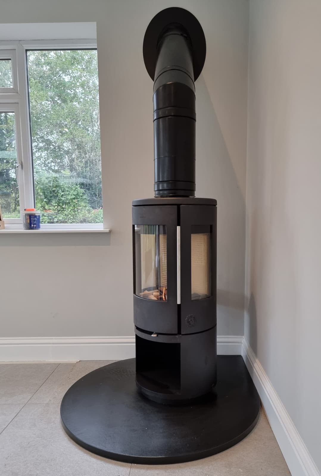 Freestanding pedestal stove positioned beside a full-height window