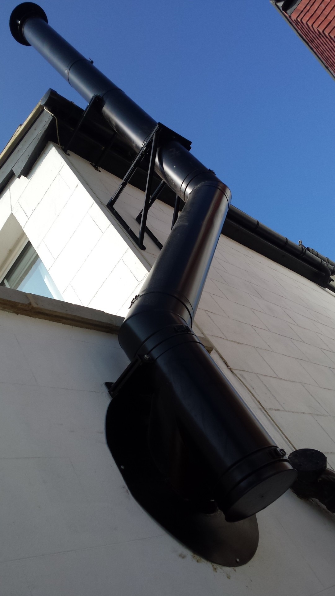Black twin-wall flue system running up a rendered gable wall past the roof line