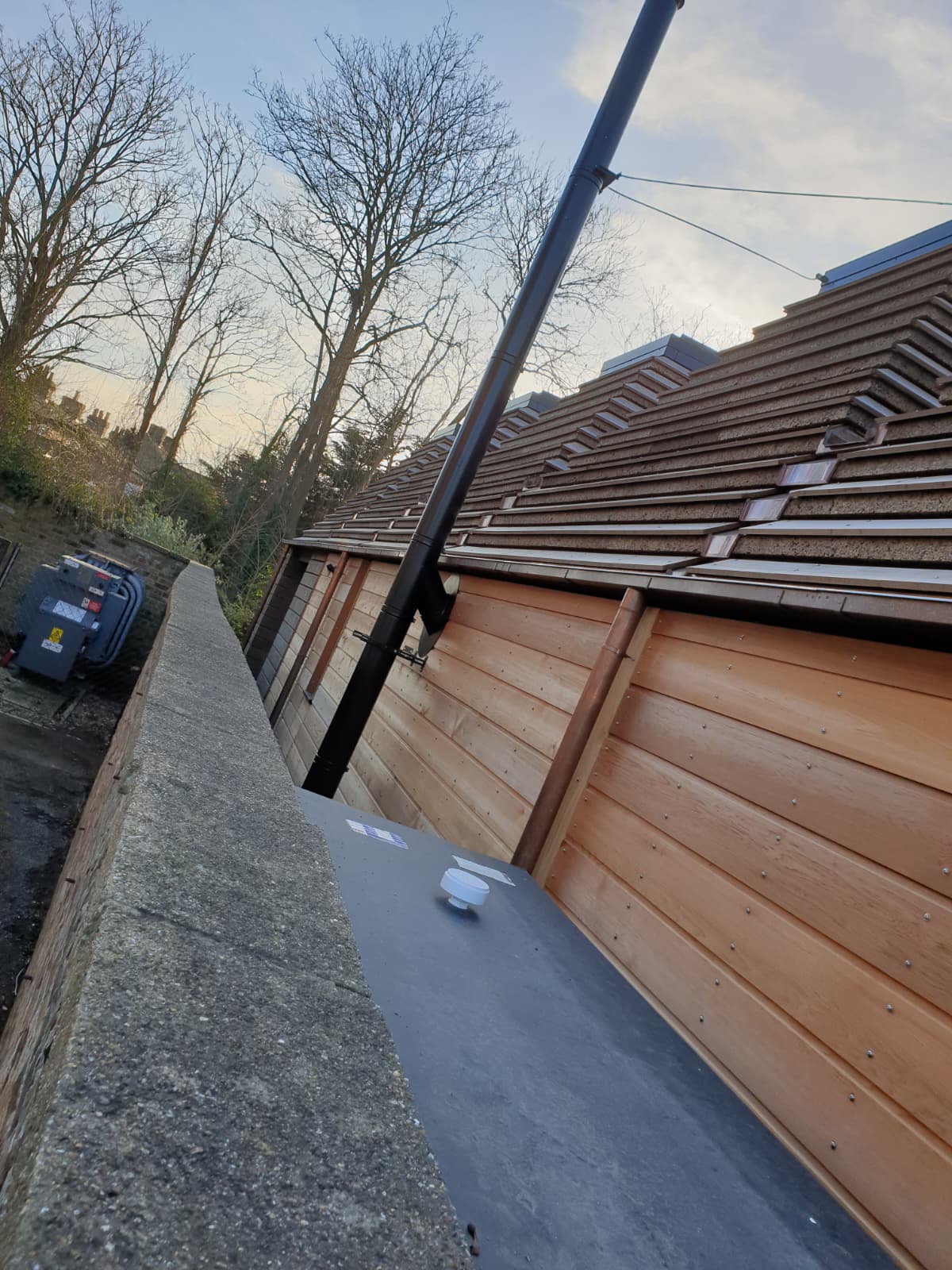 External black twin-wall flue installation rising up a timber-clad building