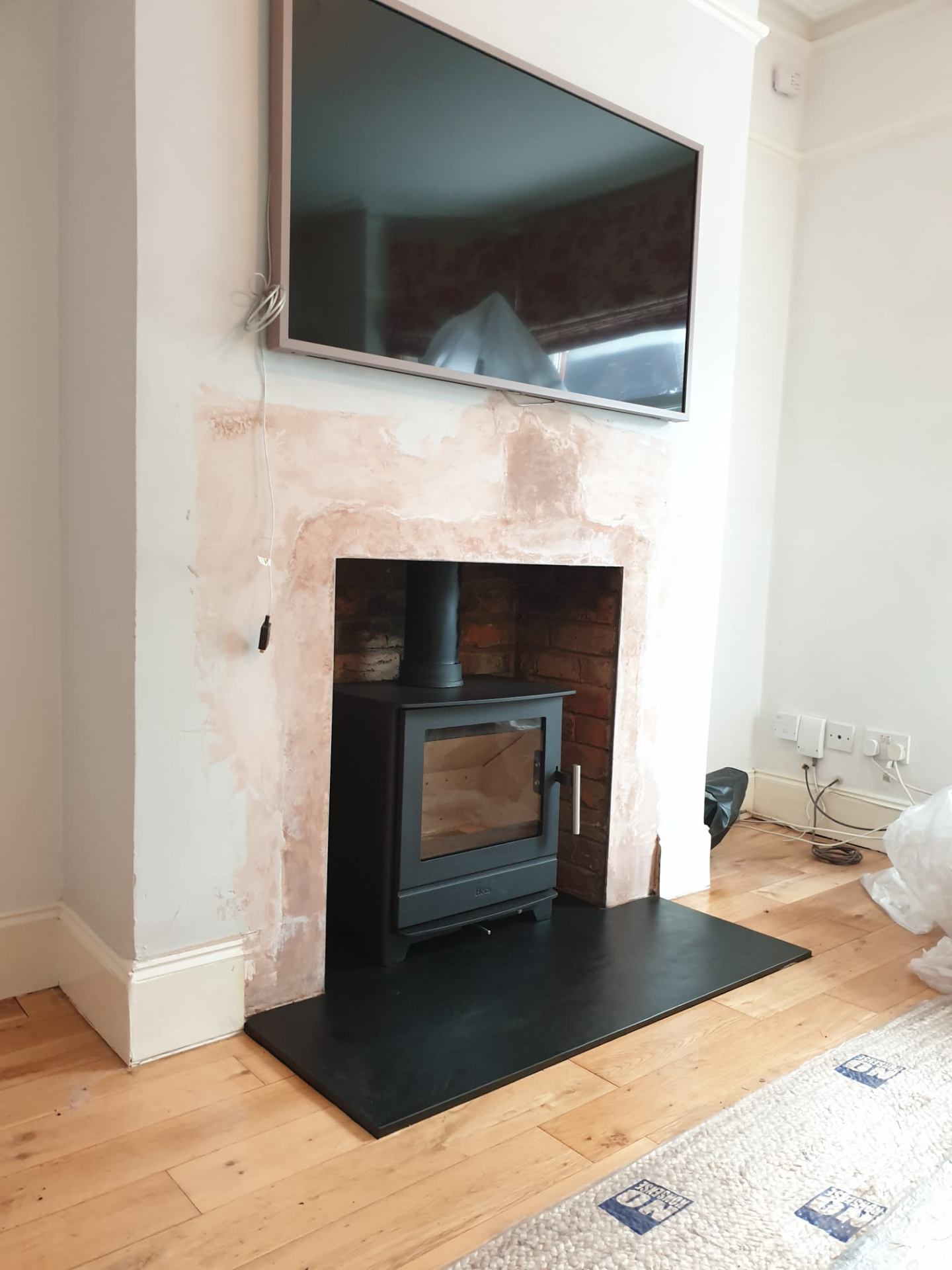 Media wall with wall-mounted TV above a freestanding stove on a brick feature wall