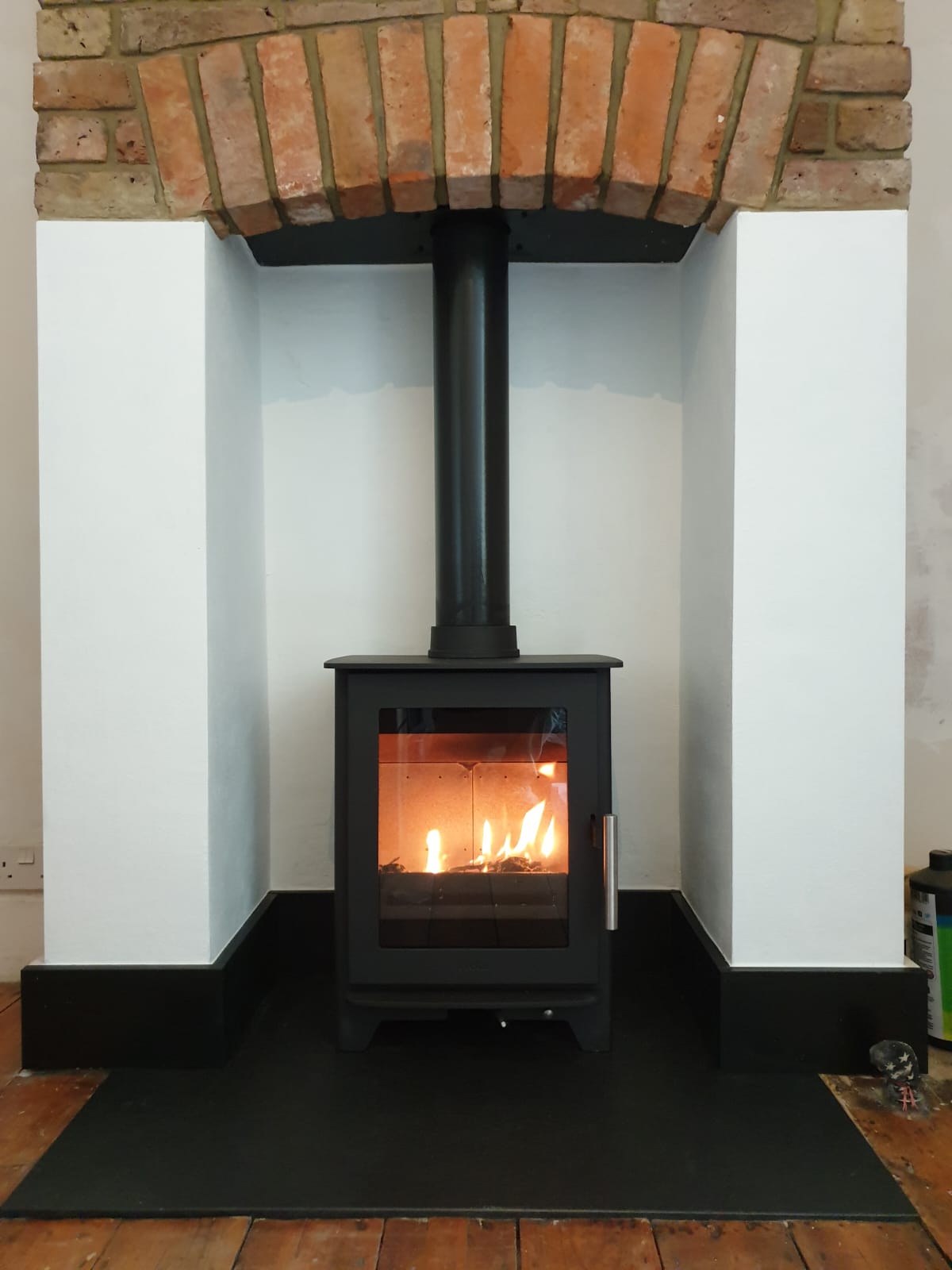 Inset stove installation within a white chimney breast and brick arch