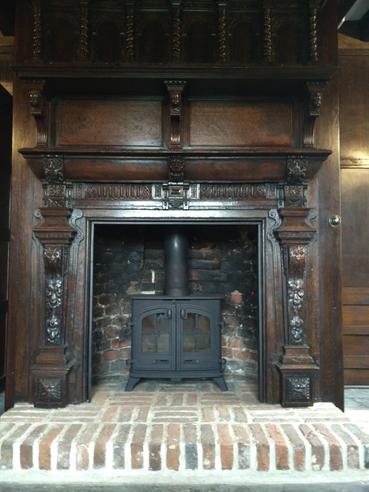 Restored large carved dark timber mantel housing a period cast iron stove