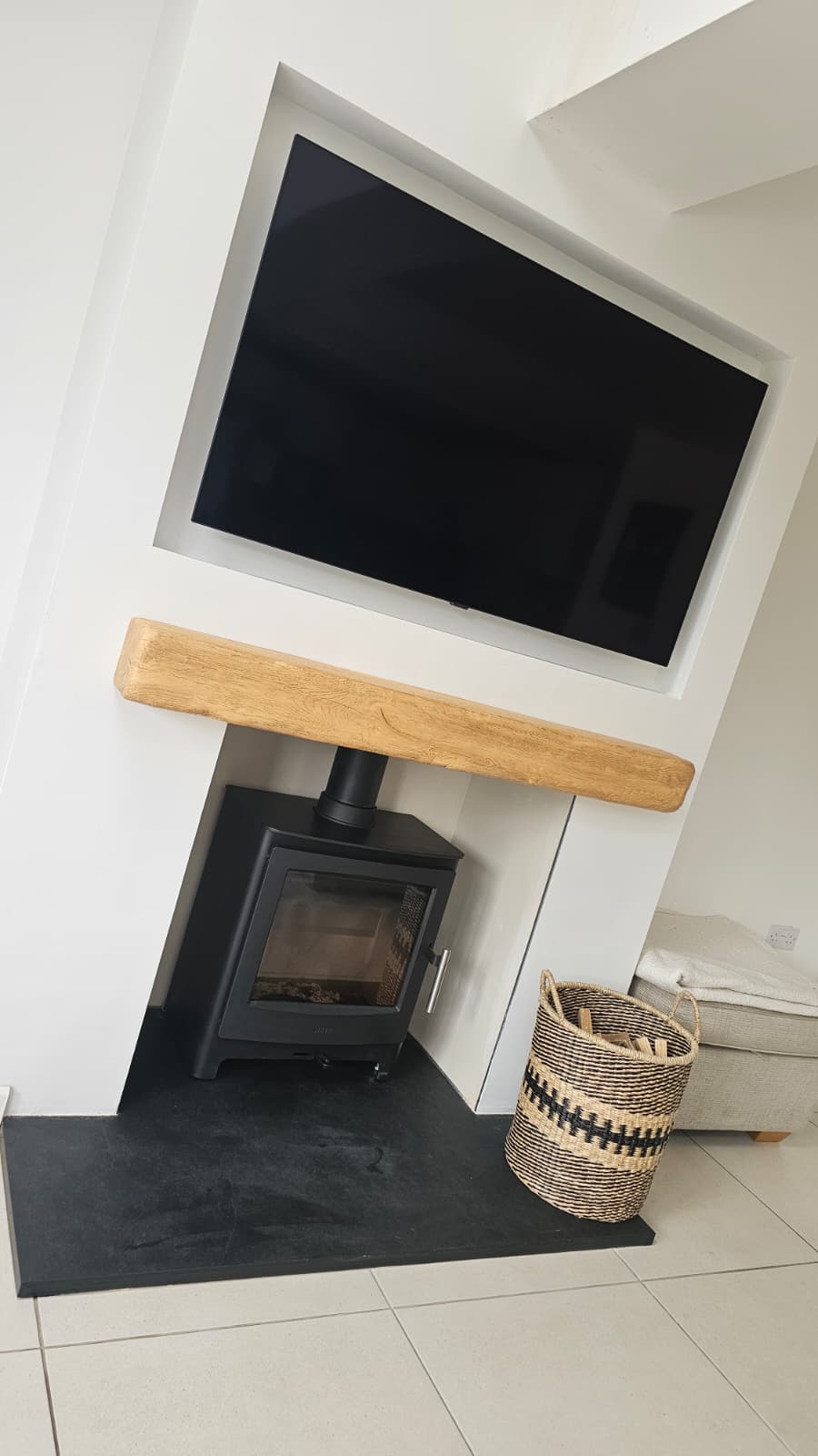Media wall installation with inset TV above an oak beam and wood burning stove