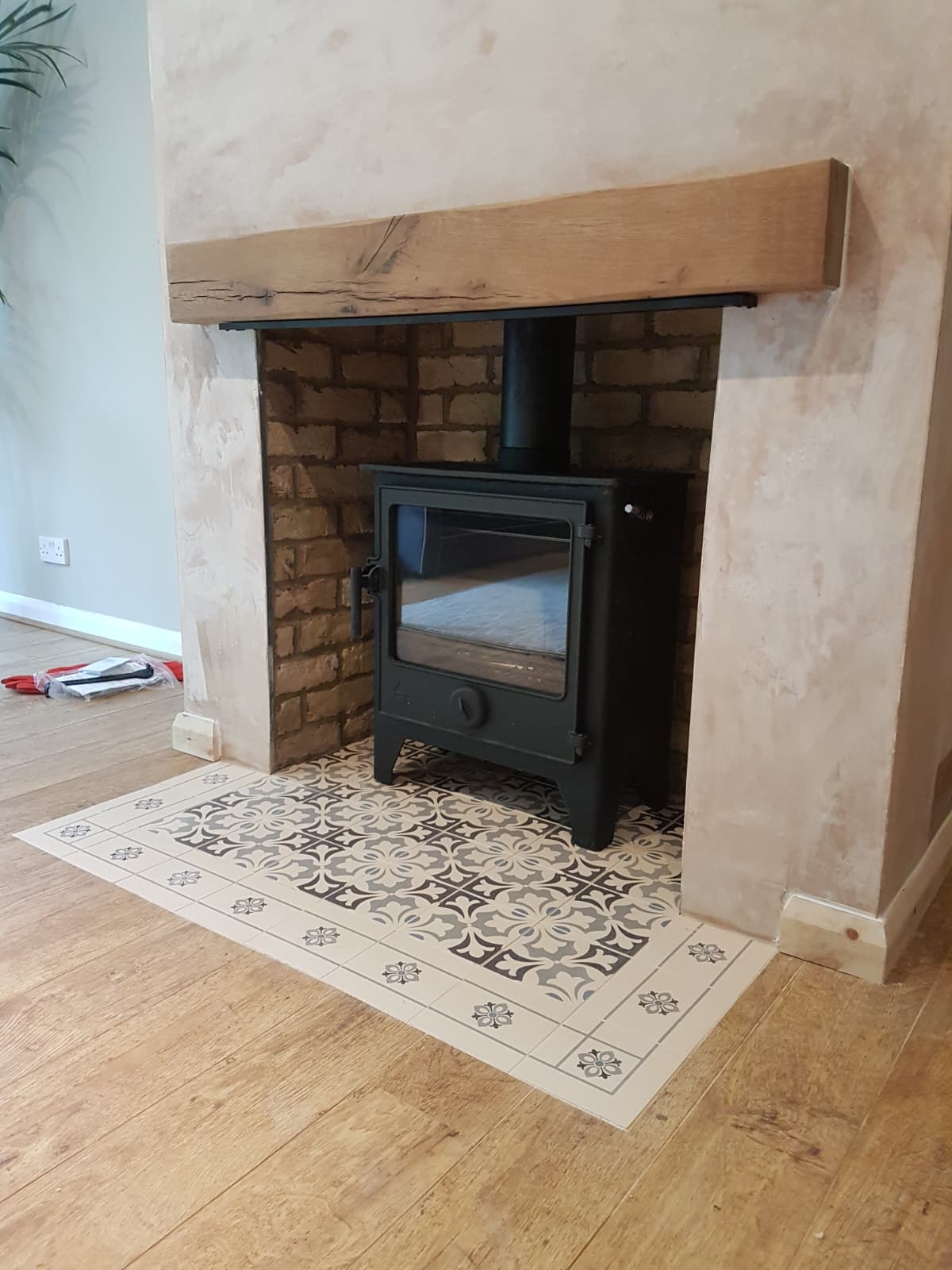 Wood burning stove in a brick recess with rustic oak beam and patterned tile hearth